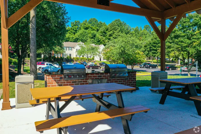Charming outdoor BBQ area with picnic tables, grills, and lush greenery.