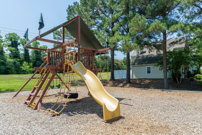 Inviting playground area featuring a wooden playset with a slide, swings, and ladder nestled among lush trees.