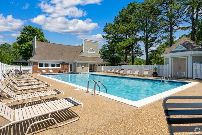 Charming outdoor pool area with lounge chairs, surrounded by lush greenery and a cozy clubhouse.