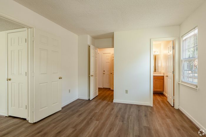 Spacious bedroom with wooden flooring, neutral walls, and ample natural light.