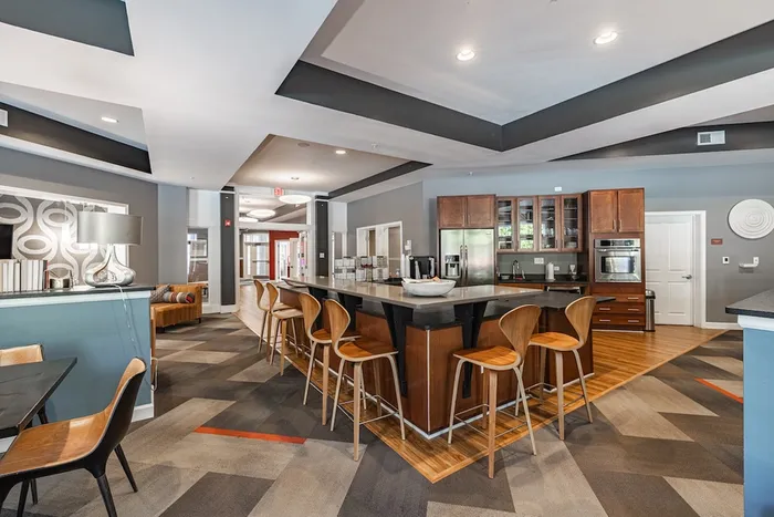 Modern communal space with a stylish kitchen, bar seating, and cozy lounge area in a contemporary apartment building.