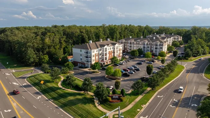 Aerial view of modern apartment complex surrounded by lush greenery, with ample parking and scenic pathways.