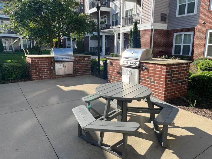 Charming outdoor patio with modern grills and cozy seating, perfect for social gatherings in a serene apartment complex setting.