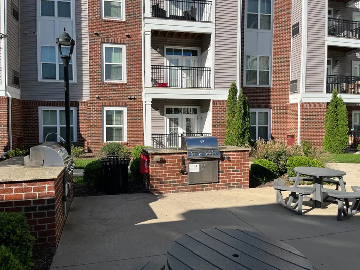 Charming apartment exterior with a modern brick facade, featuring a communal outdoor space with a barbecue grill and picnic tables.