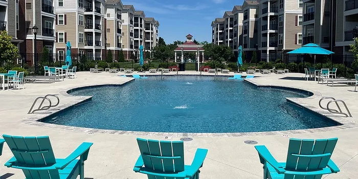 Luxurious apartment complex featuring a crystal-clear swimming pool surrounded by stylish turquoise lounge chairs and umbrellas, perfect for relaxation and leisure.