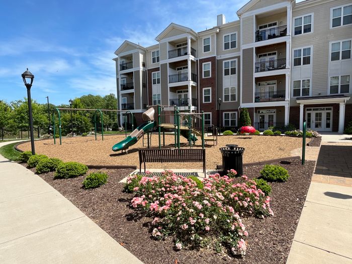 Charming apartment complex with a vibrant playground, surrounded by lush greenery and blooming flowers, perfect for family living.