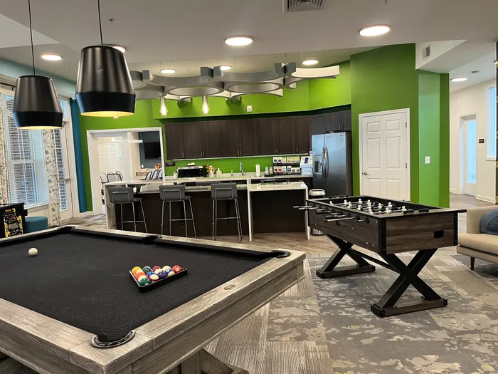 Modern recreational space featuring a stylish kitchen, pool table, and foosball, accented by vibrant green walls and chic lighting.