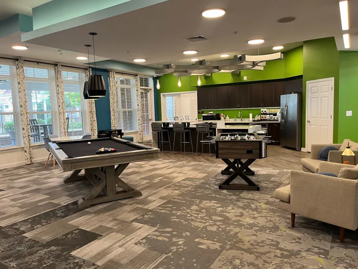Modern recreation room with a pool table, foosball table, stylish seating area, and a sleek kitchen with vibrant green accents.
