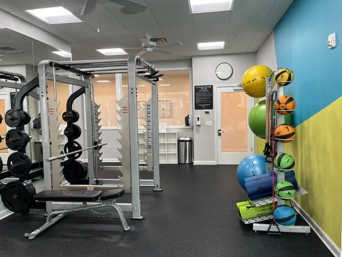 Modern fitness center with free weights, bench press, colorful exercise balls, and sleek mirrored walls for an energetic and vibrant workout experience.