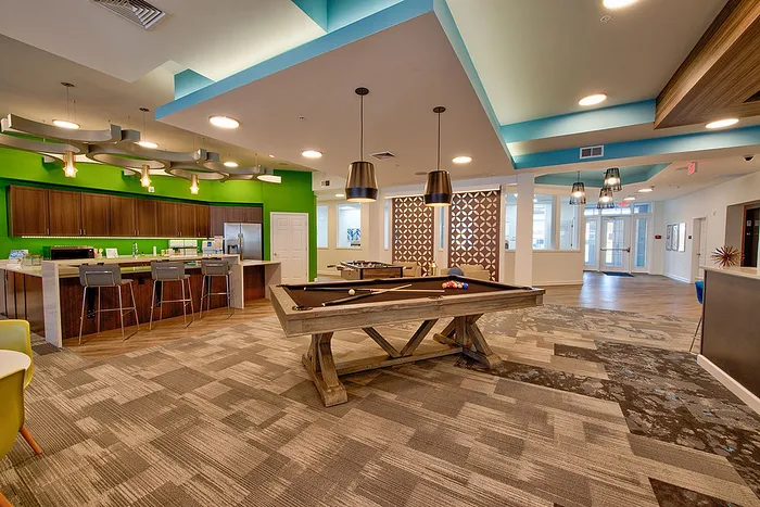 Vibrant lounge featuring a modern kitchen, bar seating, and a stylish billiards table, offering an inviting space for socializing and relaxation.