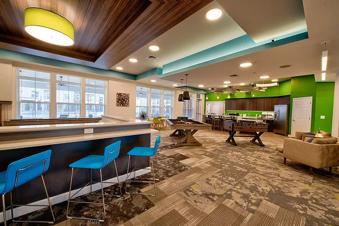 Chic apartment common area with modern bar seating, vibrant green accents, and spacious lounge, ideal for entertaining.