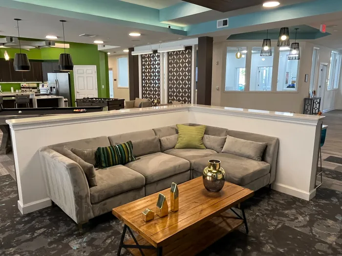 Modern and inviting community lounge area featuring a cozy grey sectional sofa, vibrant green accents, and a chic open kitchen in the background.