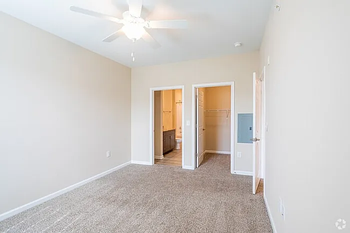 Bright and spacious bedroom featuring plush carpeting, a ceiling fan, and direct access to an en-suite bathroom with ample closet space.