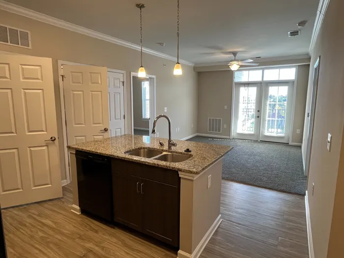 Modern apartment with open-concept layout, featuring a sleek kitchen island and bright living area leading to balcony doors.