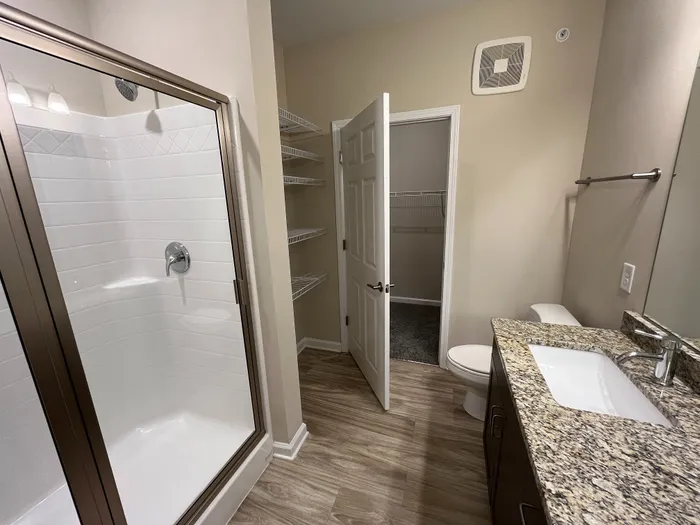 Modern bathroom featuring a sleek glass-enclosed shower, granite countertop, and ample shelving for storage.