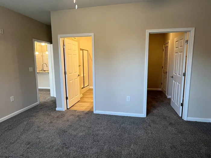 Inviting apartment interior with plush carpet, showcasing a hallway view with doors leading to a modern bathroom and a cozy bedroom.