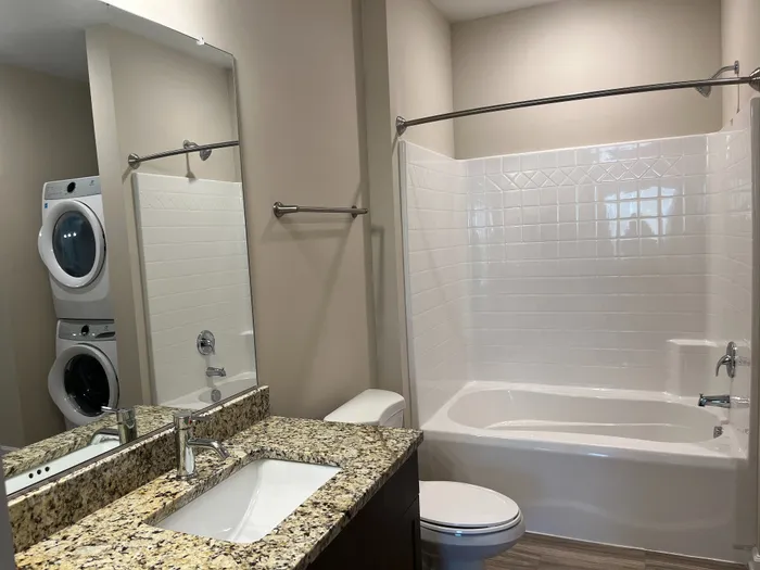 Modern bathroom featuring elegant granite countertop, sleek fixtures, and convenient in-unit stacked washer and dryer.
