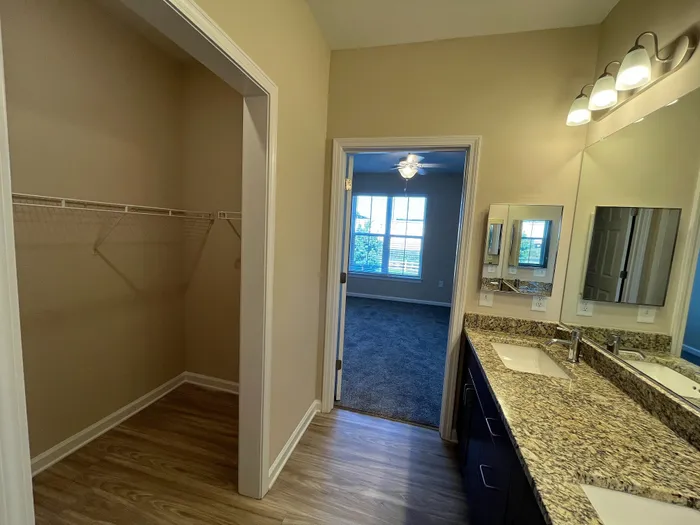 Luxurious apartment bathroom featuring elegant granite countertops, dual sinks, and a spacious walk-in closet with wooden flooring.