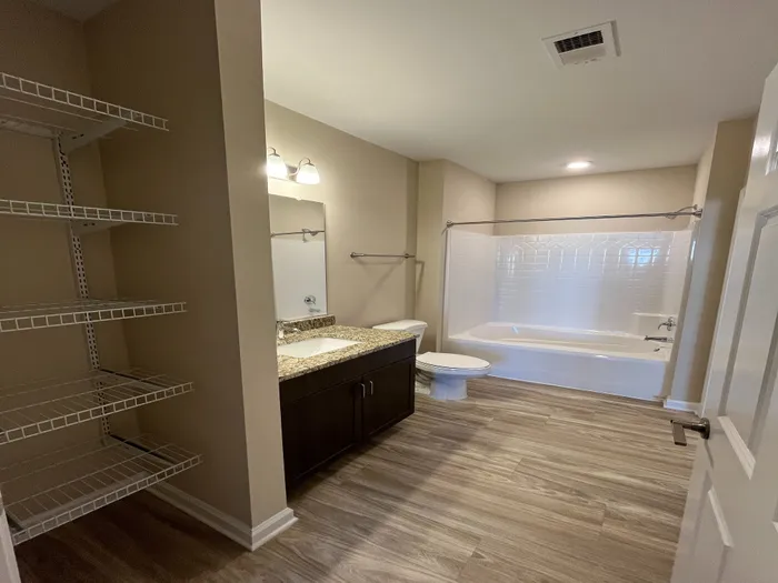 Inviting bathroom with elegant granite countertop, modern fixtures, ample shelving, and a luxurious bathtub.