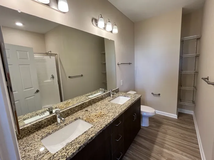 Modern bathroom featuring elegant granite countertops, dual sinks, a large mirror, and sleek wood flooring.