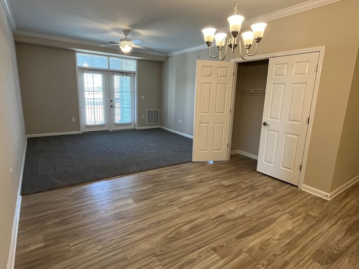 Elegant apartment interior featuring a bright open space with wooden floors, carpeted area, ceiling fan, chic chandelier, and double doors leading to a balcony.