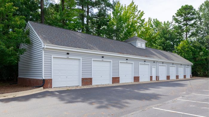 Charming row of garages with classic grey siding and brick accents set against a lush green backdrop.