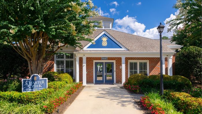 Charming brick building with a blue and white pineapple emblem, set amidst vibrant greenery and colorful flowers at Charter Creek Information Center.