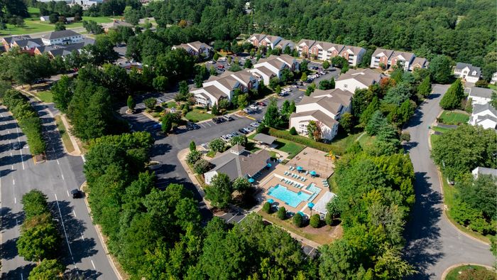 Scenic aerial view of a vibrant community with modern apartment buildings, lush greenery, and a sparkling swimming pool.