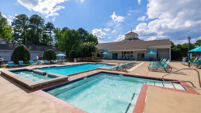 Inviting swimming pool area with lounge chairs and vibrant umbrellas, surrounded by lush greenery under a bright blue sky.