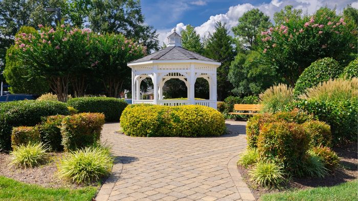 Charming garden gazebo surrounded by vibrant greenery and flowering trees, perfect for serene outdoor relaxation.