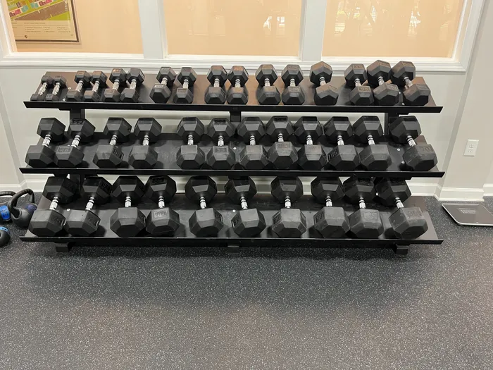 Versatile gym with a wide array of dumbbells neatly organized on a rack, offering ideal fitness opportunities in a modern apartment complex.