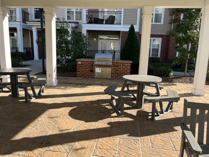 Inviting outdoor patio area with modern picnic tables and a sleek stainless steel grill, perfect for entertaining guests in a stylish apartment complex.