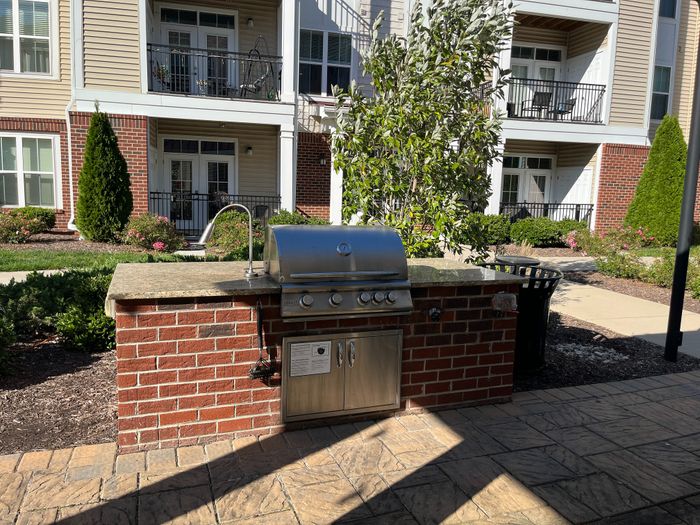 Elegant outdoor grilling station in a landscaped patio setting, framed by modern apartment balconies.