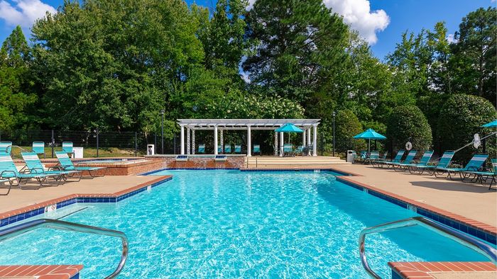 Inviting outdoor pool area with sun-drenched lounge chairs and elegant pergola surrounded by lush greenery.