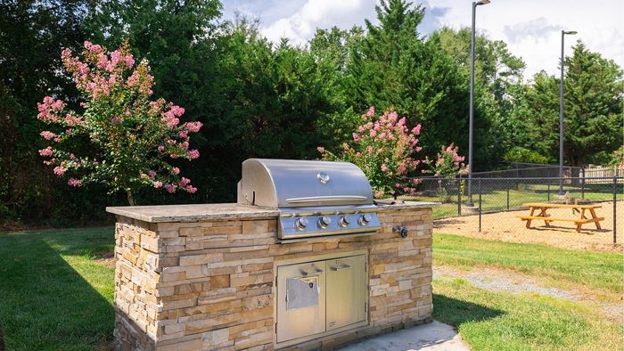 Charming outdoor barbecue area with a stone grill, surrounded by lush greenery and blooming pink flowers, perfect for entertaining.