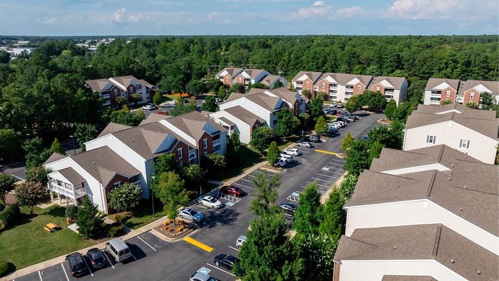 Scenic aerial view of a charming apartment complex surrounded by lush greenery, spacious parking, and well-maintained pathways.
