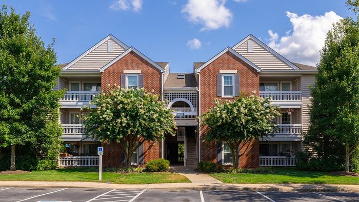 Charming apartment building surrounded by lush greenery, featuring inviting balconies and a classic brick facade under a bright blue sky.