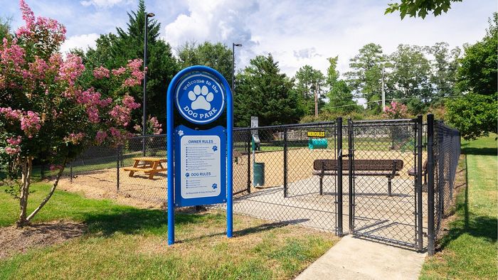 Vibrant dog park with welcoming sign, lush greenery, and cozy benches, perfect for pet-friendly community living.