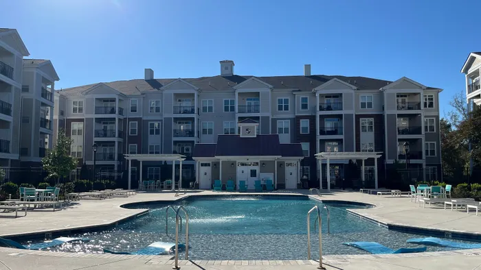 Elegant apartment complex featuring a glistening outdoor pool surrounded by stylish seating and lush greenery, perfect for relaxation and leisure.