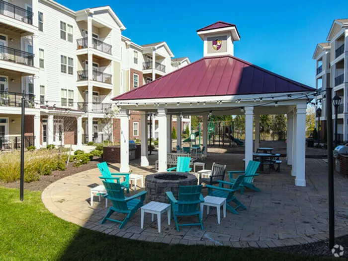 Inviting outdoor gazebo area with vibrant turquoise chairs surrounding a central fire pit, set against modern apartment buildings.