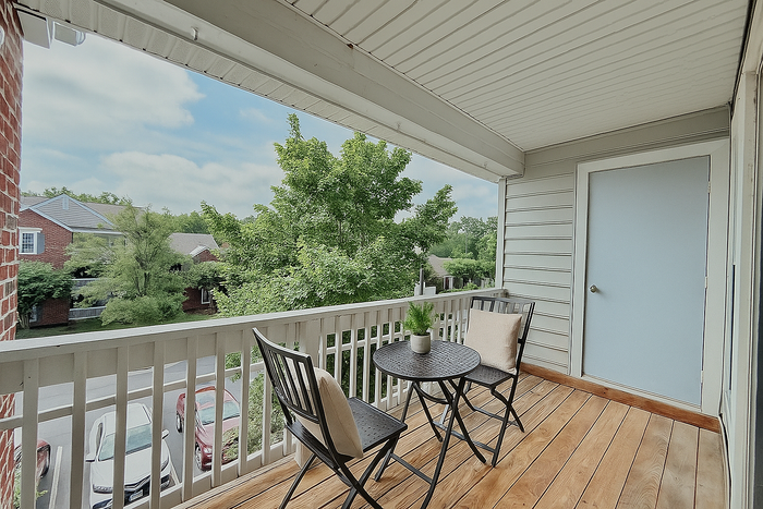 Charming apartment balcony with stylish seating, overlooking lush green trees and a serene neighborhood view.