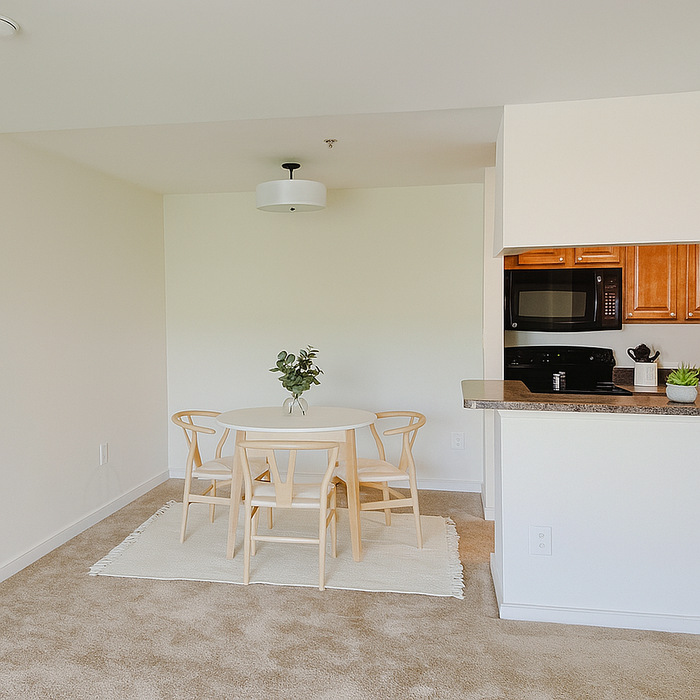 Charming dining area with a round table and chairs beside a modern kitchen featuring sleek appliances and wood cabinets. Bright, inviting space ideal for intimate gatherings.