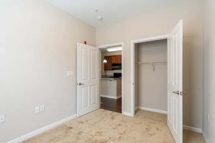 Inviting bedroom with cozy carpeting, ample closet space, and a view into a modern kitchen with sleek cabinetry.