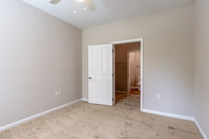 Bright, cozy bedroom with plush carpet and neutral walls, featuring a walk-in closet and adjoining bathroom.