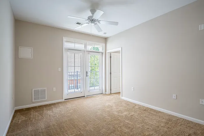 Bright and inviting bedroom with plush carpet, modern ceiling fan, and large windows opening to a private balcony.