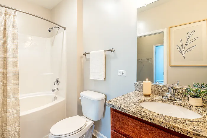 Elegant bathroom with modern fixtures, featuring a sleek granite countertop, a decorative candle, and a soothing bathtub with a striped curtain.