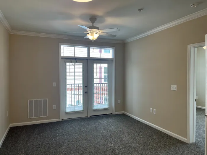 Inviting living room with plush carpeting, large windows, and a modern ceiling fan, offering ample natural light.