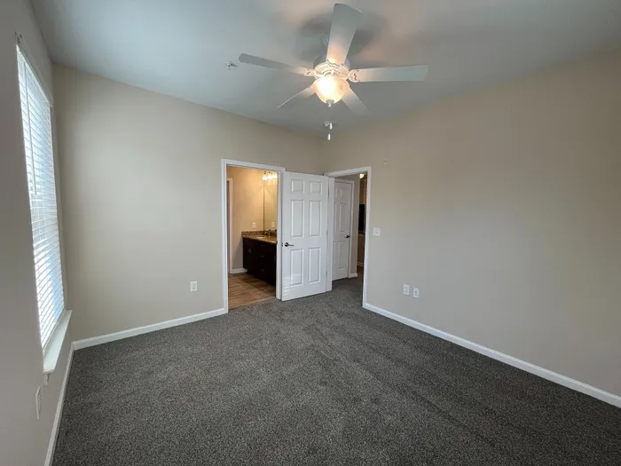 Bright bedroom with cozy carpeting, a ceiling fan, and an ensuite bathroom, offering a comfortable and inviting living space.