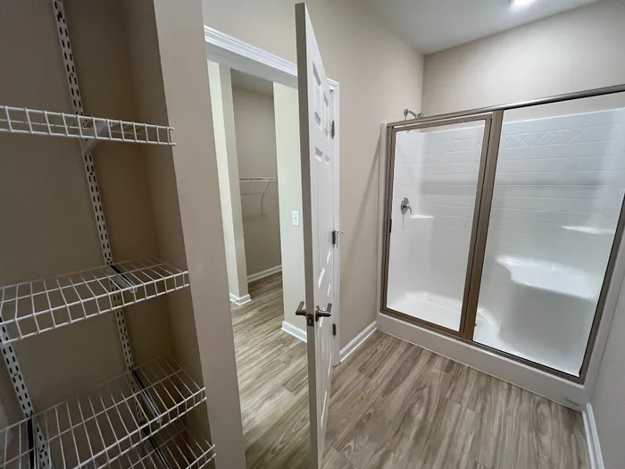 Bright and modern bathroom with a sleek glass-enclosed shower, elegant wood-textured flooring, and convenient wire shelving.