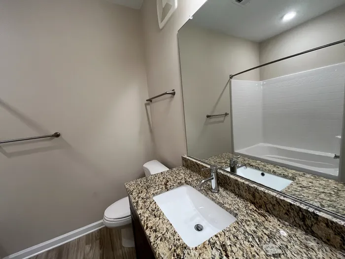 Modern bathroom featuring elegant granite countertops, sleek fixtures, and a spacious shower-tub combo under soft lighting.